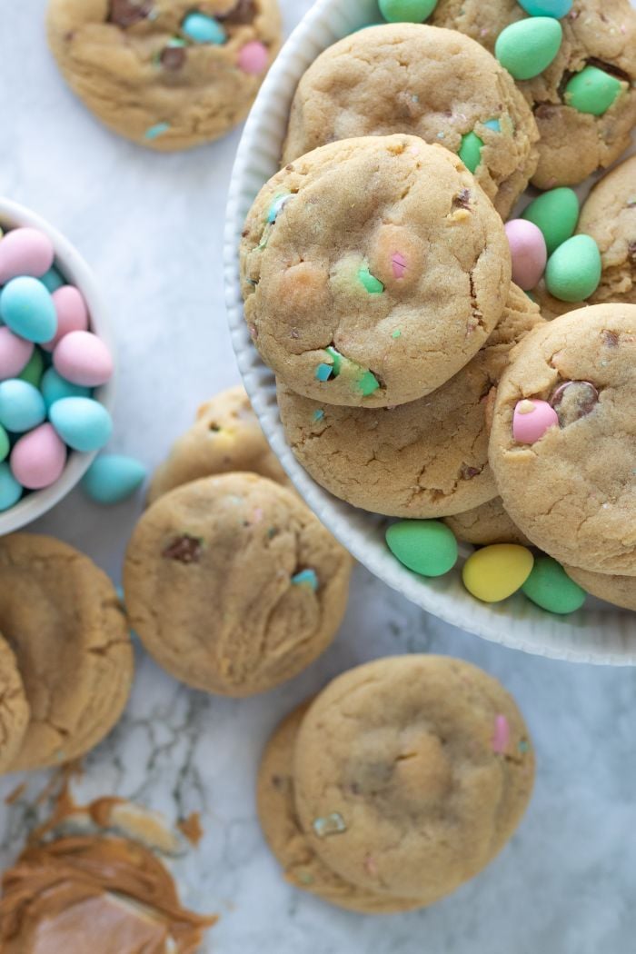 Cookies are shown on a platter, below is a bowl of mini eggs and some more cookies scattered